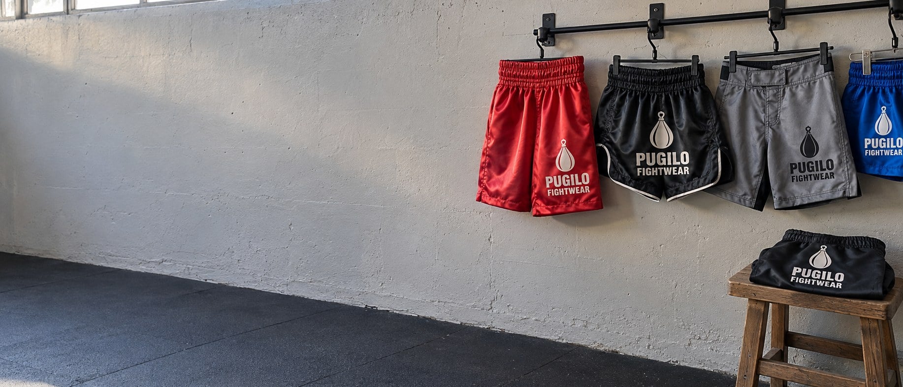 Custom satin boxing shorts, Muay Thai shorts and fight shorts hanging on gym hooks above a wooden stool